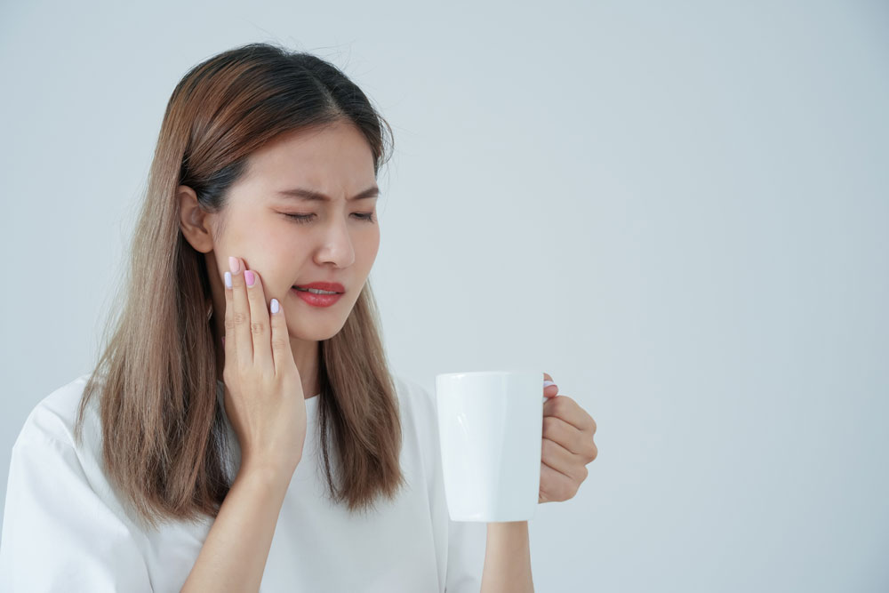 A woman drinking hot coffee is experiencing pain because hot drinks are one of the causes of tooth sensitivity.