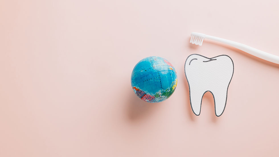 Three toothbrushes are set brush-side-up on a marble countertop, each topped with different weird toothpaste flavors from around the world.