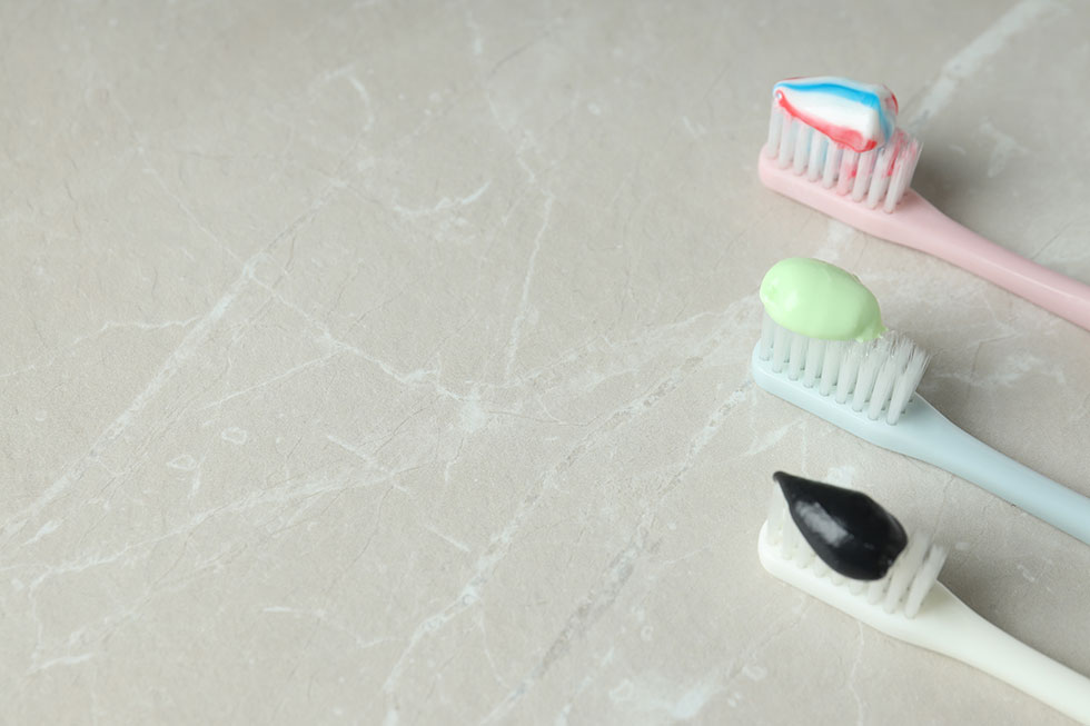 Three toothbrushes are set brush-side-up on a marble countertop, each topped with different weird toothpaste flavors from around the world.